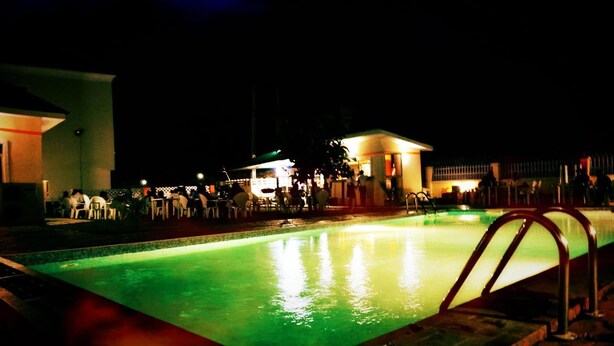 A nighttime swimming pool area with a poolside bar and lounge chairs. - Frankville Hotel (Abuja)