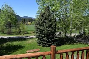 A wooden deck with a view of a green field and trees, a mountain in the background, and a clear sky. - Happy Cabin: Small Studio (Winthrop)