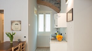 A compact kitchen with a stone arch, a dining area with a wooden table, and a white cabinet with a fruit bowl. - La Corte di Zizi-apartment 'Riva': when grandparents travel with you (Cernobbio)