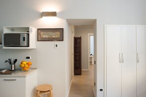 Una cocina con microondas, un tazón de fruta y un taburete de madera. Hay un cuadro enmarcado en la pared y un gabinete blanco con manija.