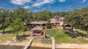 Un complexe hôtelier au bord du lac, comprenant plusieurs chalets, une terrasse couverte et un pont en bois qui enjambe l’eau.