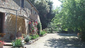 A stone building with a gravel path, potted plants, and a garden with various flowers. - Casa Crevole in Val di Merse (Murlo)