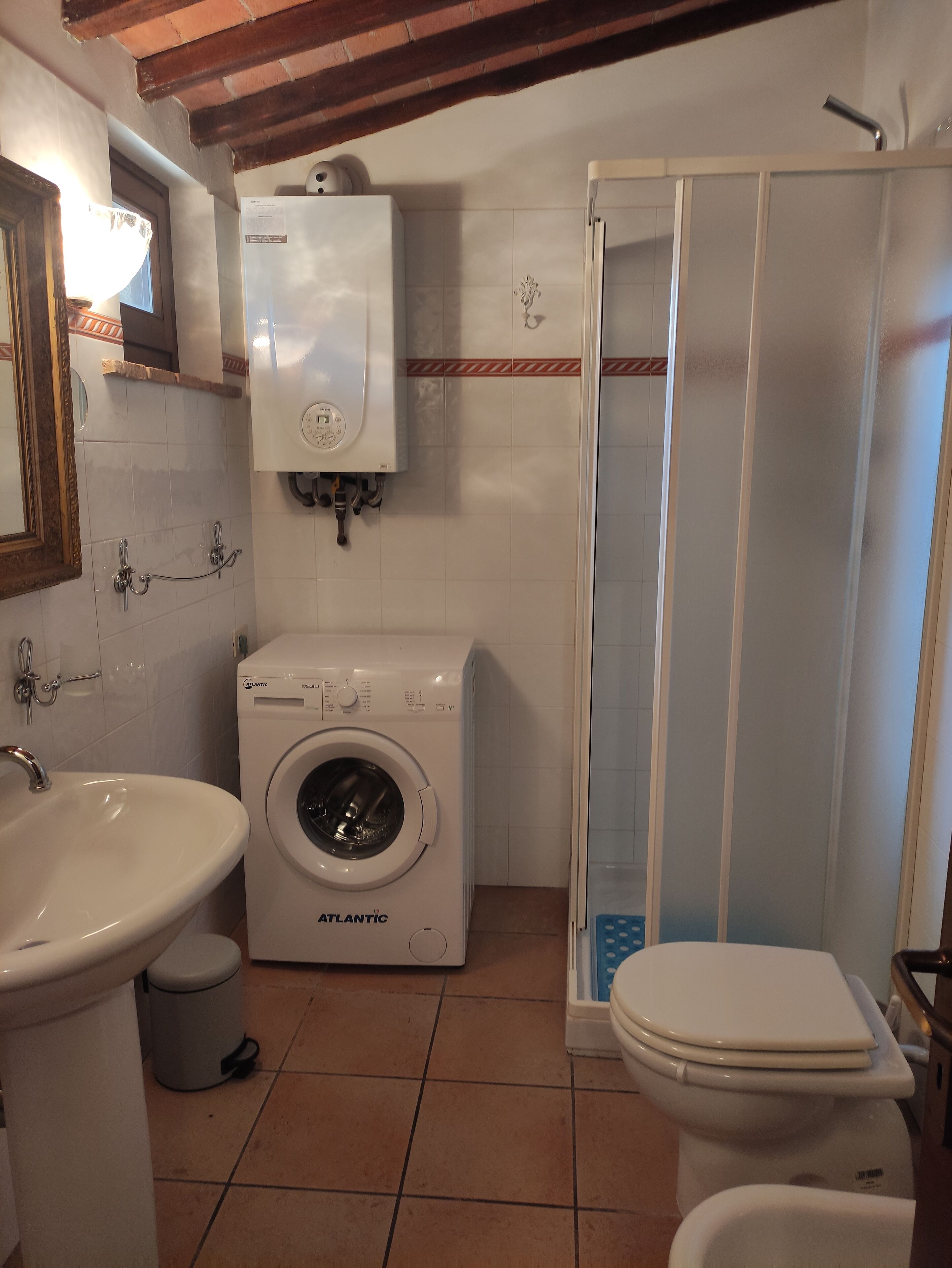 A compact bathroom with a washing machine, sink, toilet, and shower.