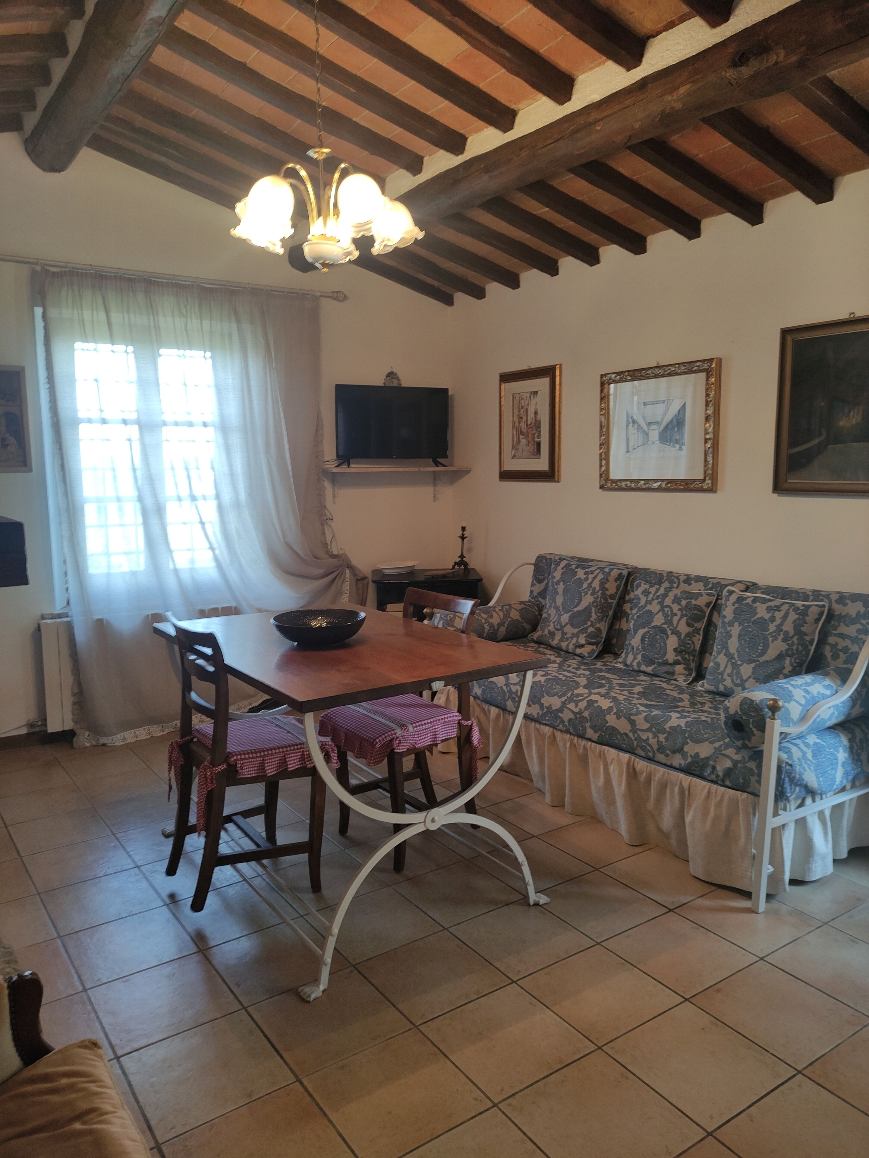 A cozy living room with a wooden ceiling, a dining table with chairs, a sofa, and a television on the wall.