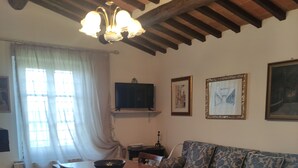 A cozy living room with a wooden ceiling, a dining table with chairs, a sofa, and a television on the wall. - Casa Crevole in Val di Merse (Murlo)