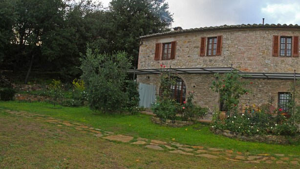 A stone building with a circular layout, multiple windows with shutters, and a garden with various plants and flowers. - Casa Crevole in Val di Merse (Murlo)