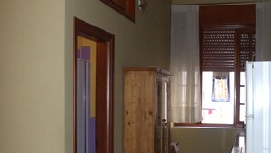 A narrow hallway with a wooden cabinet, a white refrigerator, and a window with wooden blinds. - one bedroom apartment in central location (messina)