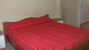 A single bed with a red striped bedspread and matching pillows, a wooden headboard, and a nightstand with a white drawer. - one bedroom apartment in central location (messina)