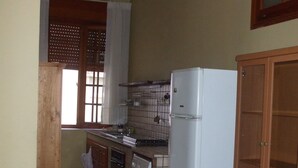 A compact kitchen with a washing machine, a refrigerator, wooden cabinets, and a window with curtains. - one bedroom apartment in central location (messina)
