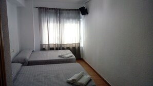 A small, clean room with two beds, a flat-screen TV mounted on the wall, and a window with sheer curtains. - Hostal Plaza de España (Salamanca)
