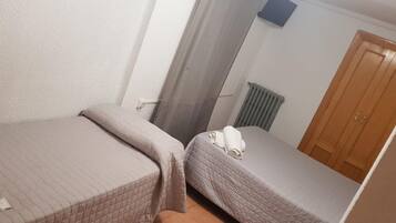 A small, single-room hotel room with two beds, a wooden door, and a radiator.