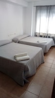 Habitación con dos camas, cada una con colchón acolchado y almohadas, y una ventana con cortinas traslúcidas.