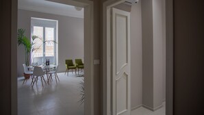 A modern interior with a dining area featuring a round table and chairs, a potted plant, and a view through an open door. - Ortigia Casa Fab Sandstone Apartment with Balcony (Siracusa)