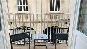 A balcony with two black chairs and a small table, a tiled floor, and a stone building with windows in the background. - Ortigia Casa Fab Sandstone Apartment with Balcony (Siracusa)