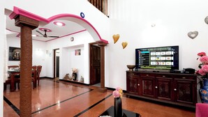 A spacious living area with a modern design, featuring a large flat-screen TV, a dining table, and a decorative vase.