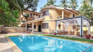 A two-story house with a swimming pool, outdoor furniture, and a covered patio area.