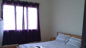 A bedroom with a single bed, a bedside table, a nightstand, a ceiling fan, and a window with curtains.