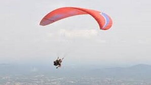A person paragliding with a red and blue parachute over a cityscape.