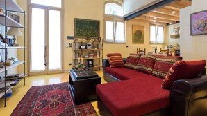 Ein Wohnzimmer mit einem roten Sofa, einem Couchtisch, einem Bücherregal und einem großen Fenster.