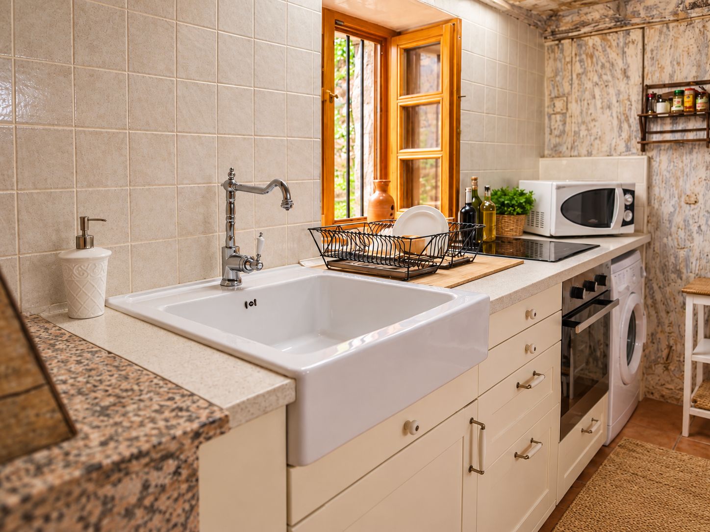 A kitchen with a white sink, stainless steel faucet, a dish rack, a microwave, and a built-in oven.