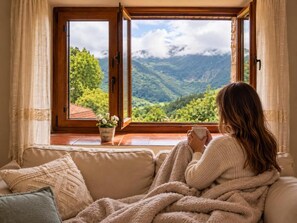 A person sitting on a sofa by a window with a view of a mountainous landscape. - Fantastic Views Over The Mountains And Peaceful (Asturias)