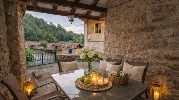 Un área de comedor al aire libre rústica con muros de piedra, una mesa de vidrio y velas.