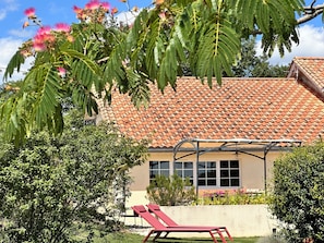 A house with a tiled roof, a covered outdoor seating area, and lush greenery.