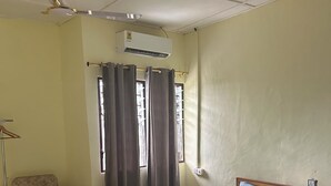 Ein Schlafzimmer mit einem Bett, einem Sessel, einem Fenster mit Vorhängen, einer Klimaanlage und einem Deckenventilator.