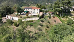 Un edificio con tetto in tegole rosse, immerso nel verde e circondato da colline.