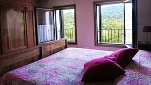 Una camera da letto con soffitto in legno, un letto con copripiumino decorato, una finestra vista sul verde e un armadio in legno.