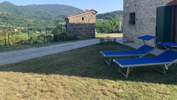 Un edificio in pietra con un vialetto sterrato che conduce a una zona verde con poltrone da relax blu.