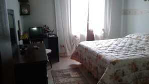 Ein Schlafzimmer mit einem Bett, einem Schreibtisch, einem Fernseher und einem Fenster mit Vorhängen.