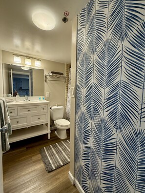 A bathroom with a white vanity, a toilet, a shower area, and a patterned wall. - 1519 · Ilikai Collection # 9. Beachfront Resort, upgraded (Honolulu)