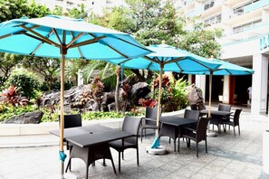 An outdoor seating area with tables and chairs, surrounded by tropical plants and a rock garden. - 1519 · Ilikai Collection # 9. Beachfront Resort, upgraded (Honolulu)