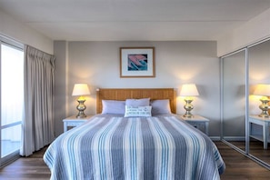 A hotel room with a large bed, two bedside tables with lamps, a framed picture on the wall, and a window with curtains. - 1519 · Ilikai Collection # 9. Beachfront Resort, upgraded (Honolulu)