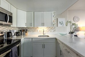 Una cocina moderna con armarios blancos, un lavamanos de acero inoxidable y un salpicadero de azulejos.