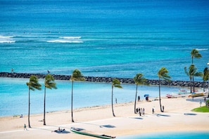A beach with palm trees, a rocky breakwater, and people walking along the shore. - 1519 · Ilikai Collection # 9. Beachfront Resort, upgraded (Honolulu)