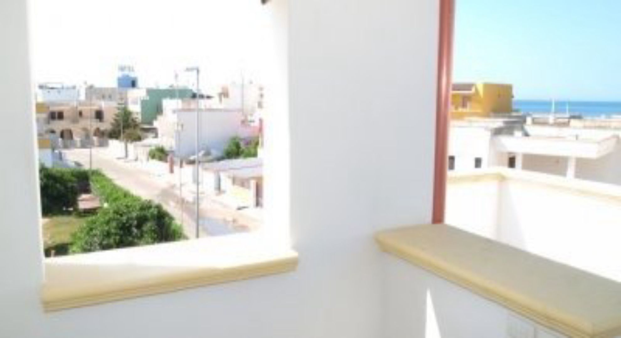 Ein Zimmer mit Fenster und Blick auf die Stadt, einer weißen Wand und einem teilweisen Balkon.