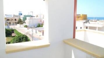 Ein Zimmer mit Fenster und Blick auf die Stadt, einer weißen Wand und einem teilweisen Balkon.