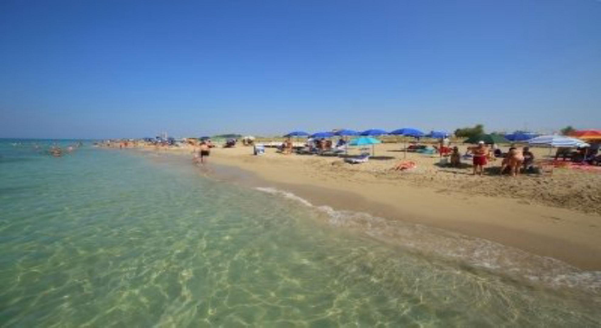 Uma praia com águas cristalinas, pessoas e guarda-sóis.