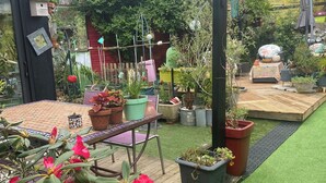 Een tuin met kunstgras, plantenpotten, een houten terras en een pergola.