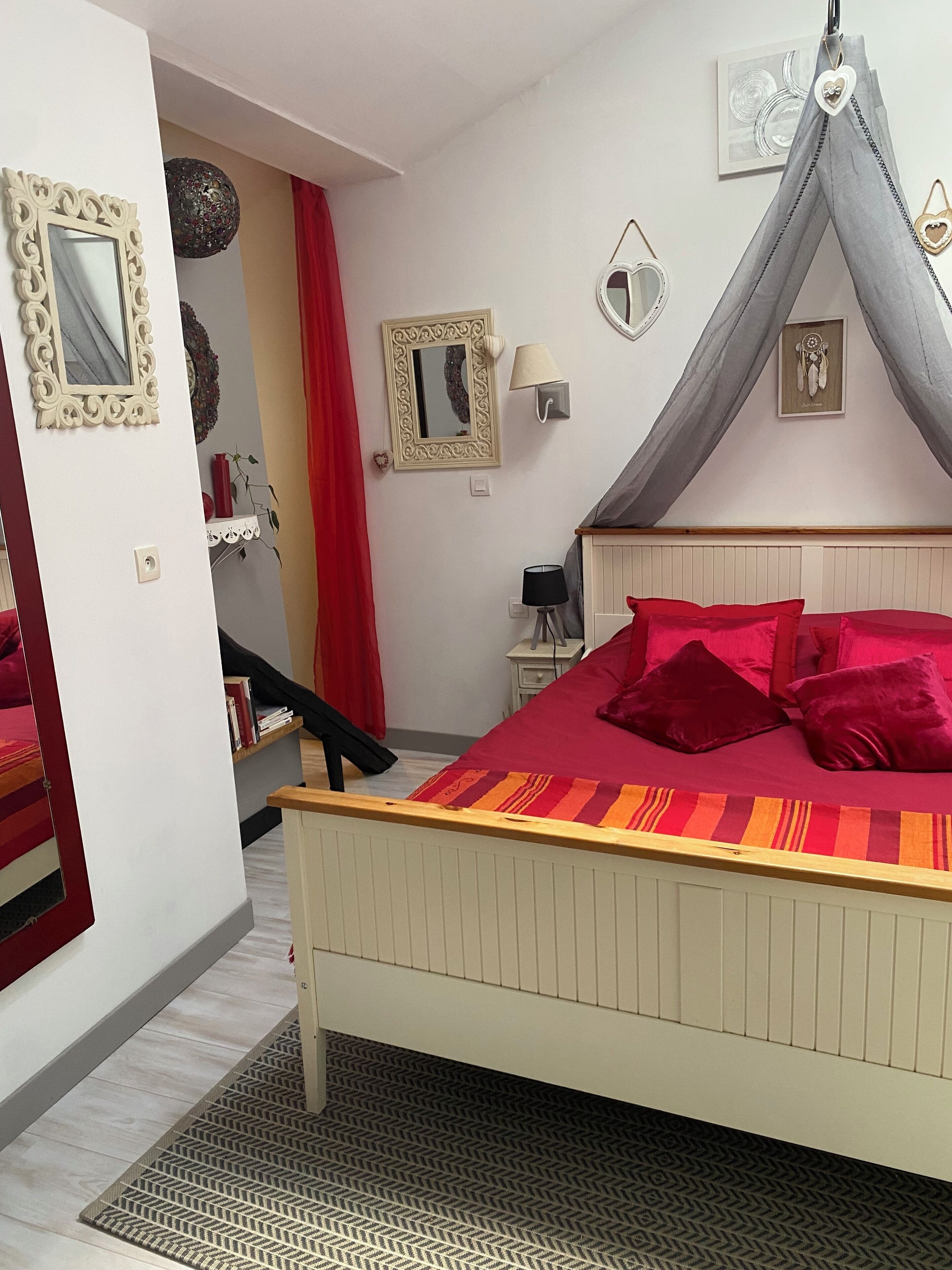 Une chambre à coucher avec un lit, une table de chevet, une lampe, un miroir et un mur orné d’un attrape-rêves.