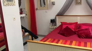 Une chambre à coucher avec un lit, une table de chevet, une lampe, un miroir et un mur orné d’un attrape-rêves.