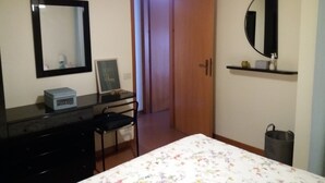 A bedroom with a bed, a dresser, a chair, a desk, a mirror, a door, and a shelf with a few items. - Villa near the sea, Cinquale Forte dei Marmi (CINQUALE)