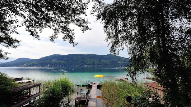 Une vue sur le lac, avec un quai en bois, un parasol jaune et un bateau.