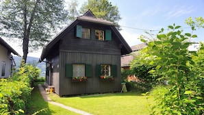 Une maison traditionnelle en bois, avec un toit à pente, des volets verts et des jardinières aux fenêtres.