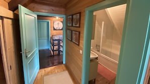 Un couloir étroit aux murs et au sol en bois, qui mène à une salle de bain équipée d’une baignoire et d’un lavabo.