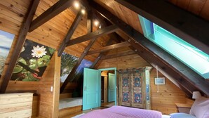 Une chambre mansardée chaleureuse, avec un plafond en pente, un lit recouvert d’une couette à carreaux, une commode en bois et un meuble décoratif.