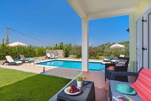Area piscina con poltroncini, un tavolo con frutta e vista sulla piscina e sul verde circostante.