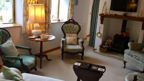 Un salon chaleureux avec un fauteuil vert, un fauteuil capitonné, une petite table ronde avec une lampe, un téléviseur et une cheminée.